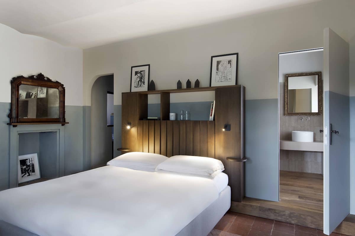 A bedroom with a bed, a wooden wardrobe, a mirror, and a bathroom door.