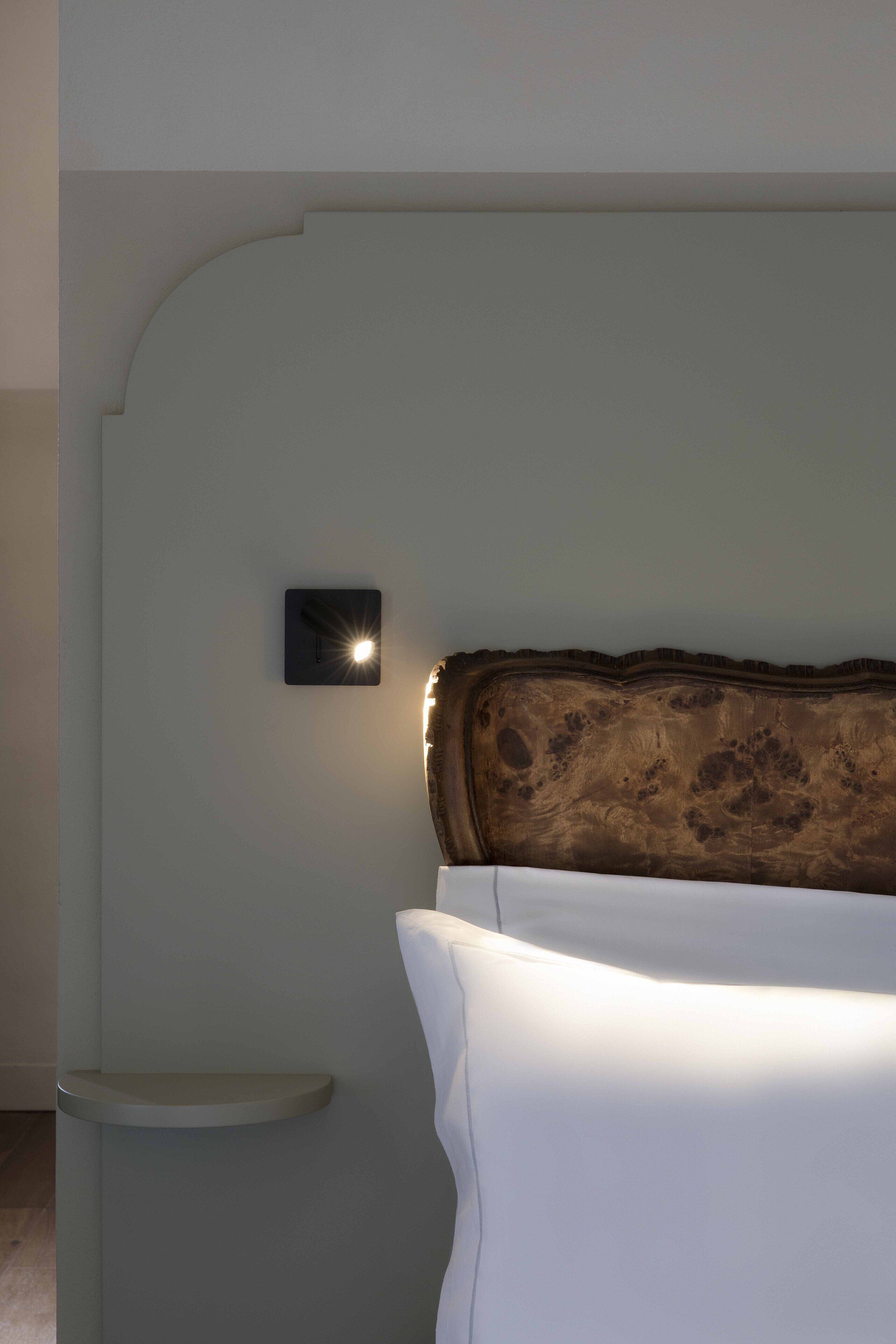 Un dormitorio con cabecera de madera, una mesita de noche y una lámpara fijada a la pared.