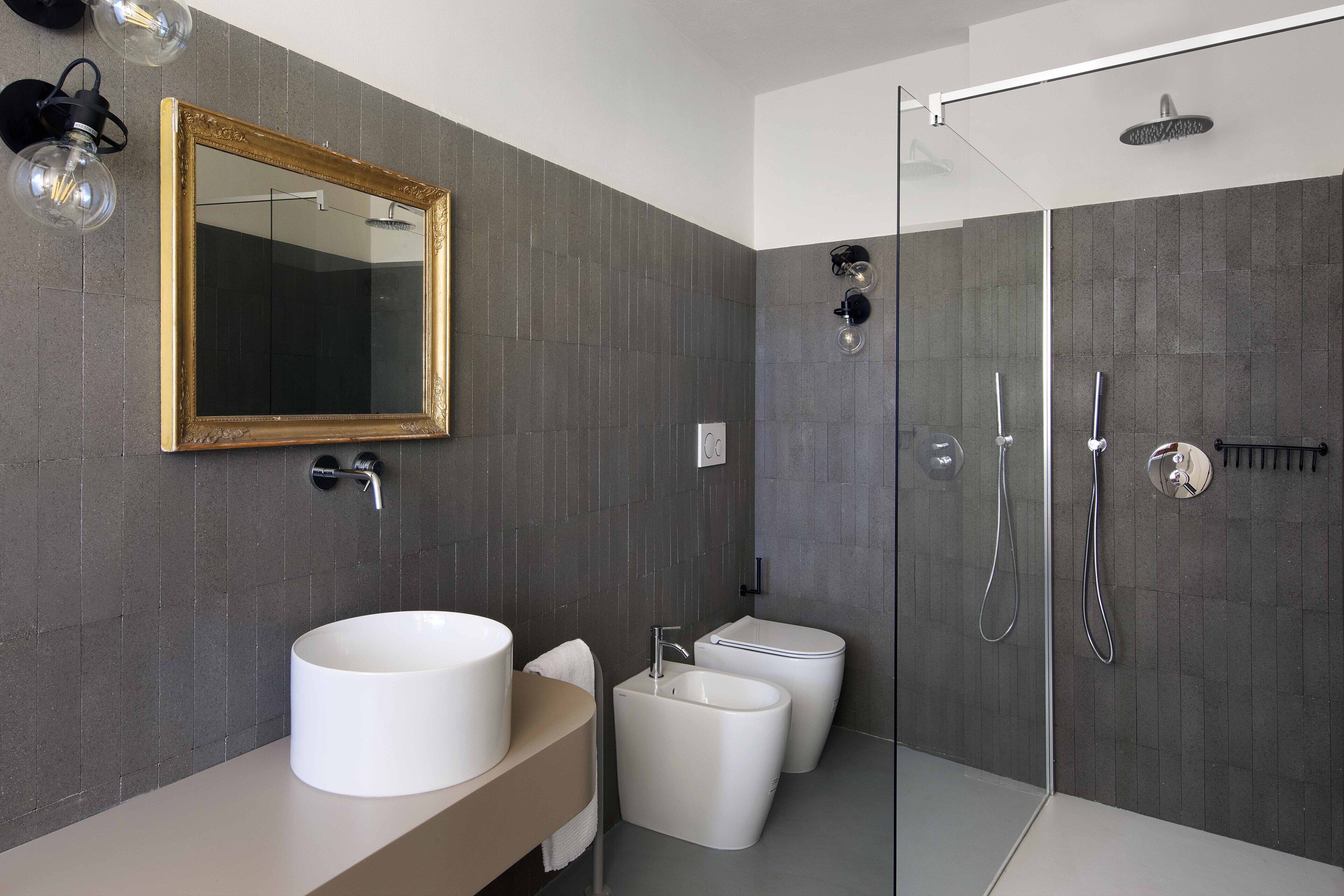 A modern bathroom with a large mirror, a round sink, a pedestal sink, and a walk-in shower.