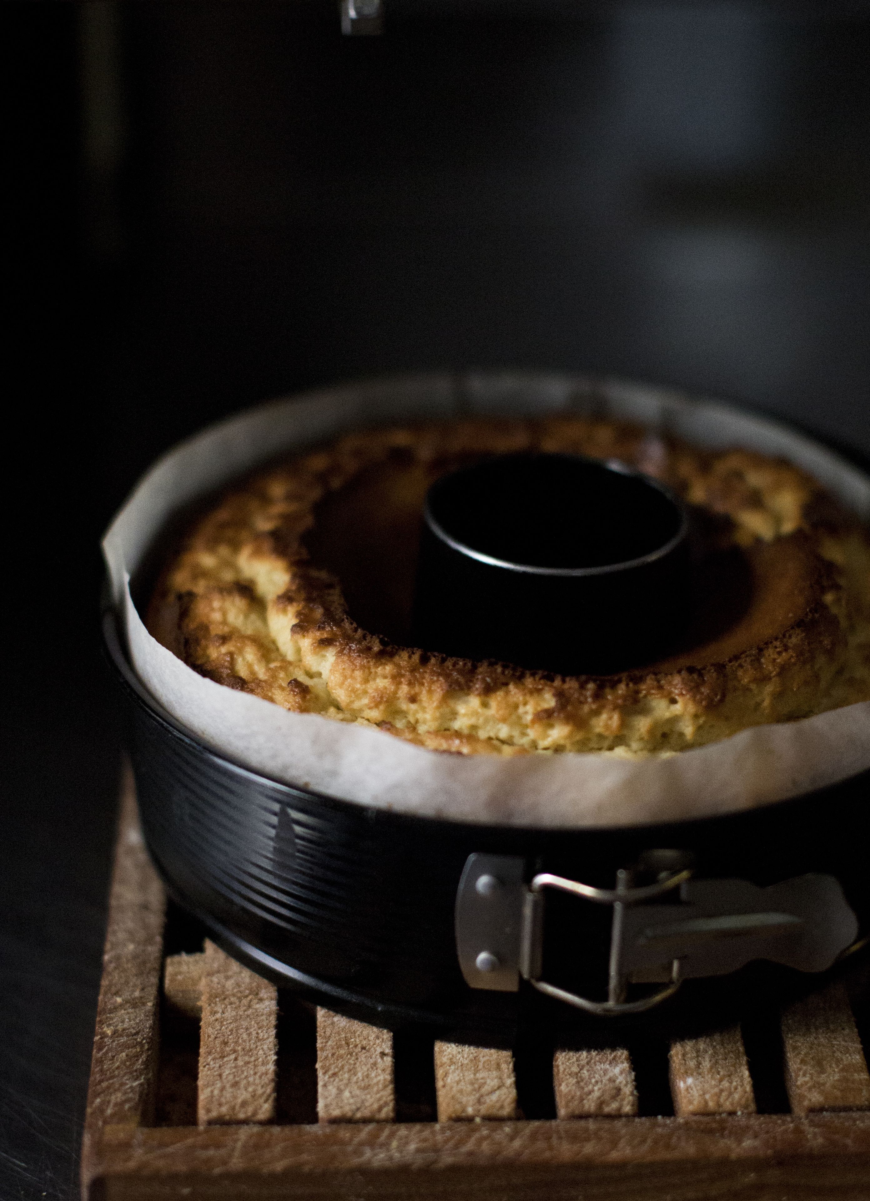 Un gâteau rond, dans un moule noir, posé sur un présentoir en bois.