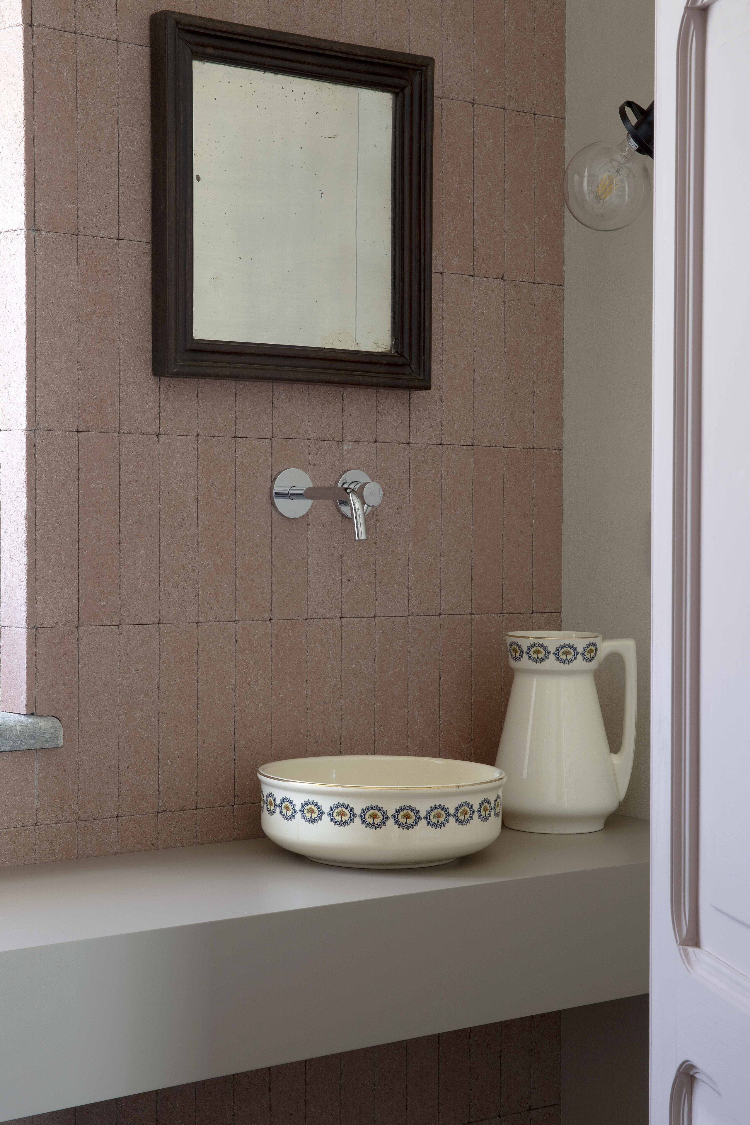 Un baño con lavamanos, espejo y jarra.