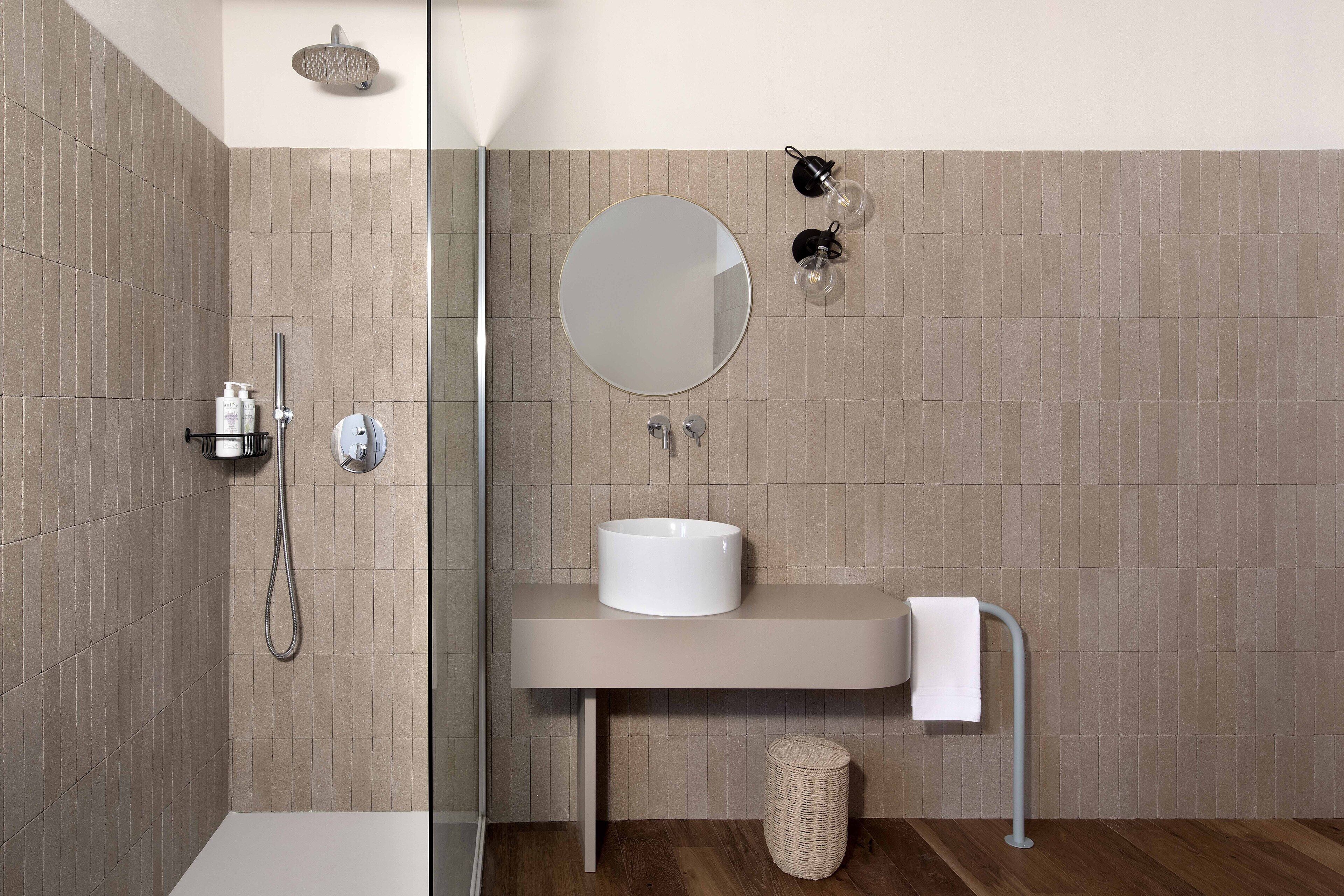 A modern bathroom with a glass shower enclosure, a round mirror, a white sink, and a towel rack.