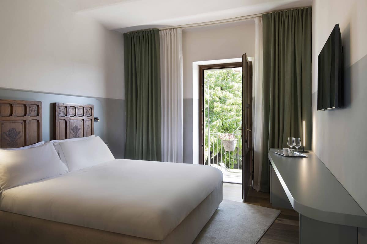 A modern hotel room with a large bed, a bedside table with a tray, and a TV mounted on the wall.