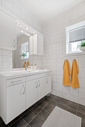 A modern bathroom with white cabinetry, a large mirror, and a window with blinds. - Modern apartment Tromsø (Tromsø)