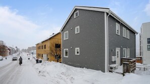 Una strada residenziale con case, una delle quali ha una facciata grigia e un portone garage visibile.