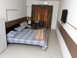 Een kleine hotelkamer met een bed, bureau, stoel, televisie en gordijn.