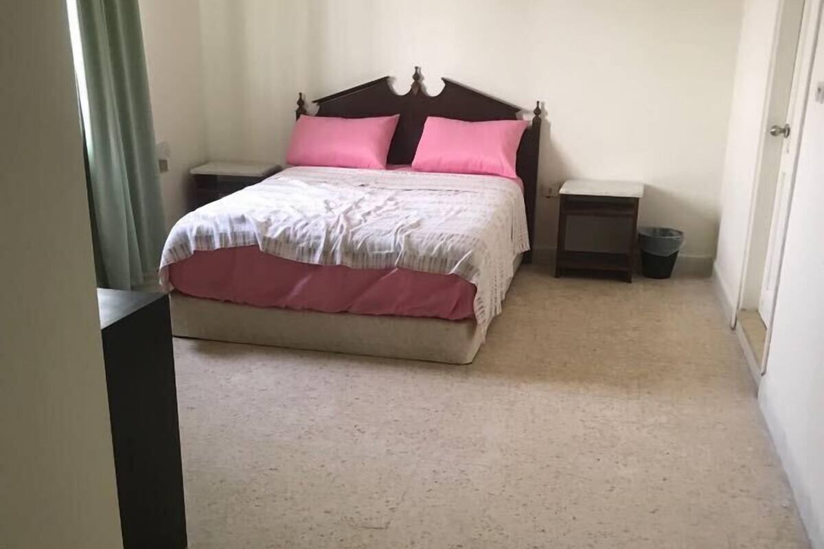 Un dormitorio con una cama, dos mesitas de noche y un cubo de basura.