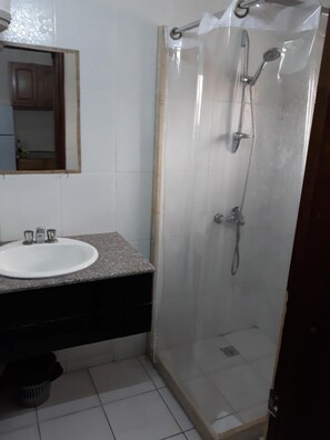 A bathroom with a white sink, dark countertop, and a glass-enclosed shower area.