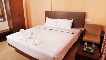 Habitación de hotel con una cama grande, un armario de madera, un sillón pequeño y una mesita de noche con botellas de agua.