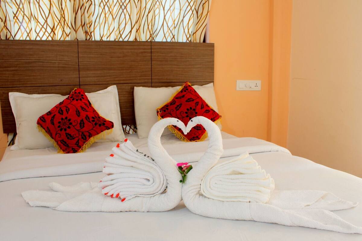 A bed with white linens, two red pillows with black patterns, and two white towels arranged in swan shapes.