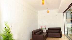 A modern living room with two brown sofas, a small green plant, and a glass partition. - Pine Tree Munnar (Devikolam)
