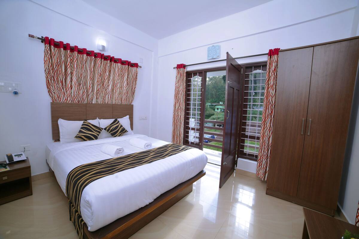 A hotel room with a bed, a wardrobe, a nightstand, and a view through the door.