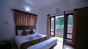 A hotel room with a large bed, a nightstand, a window with curtains, and a view of the outdoors. - Pine Tree Munnar (Devikolam)