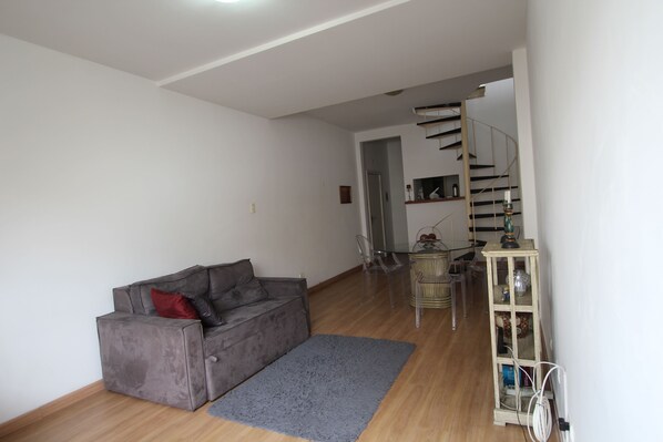 A living room with a grey sofa, a small rug, a wooden floor, a staircase, and a glass cabinet with shelves.