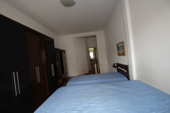 A bedroom with two beds, a wardrobe, and a painting on the wall.