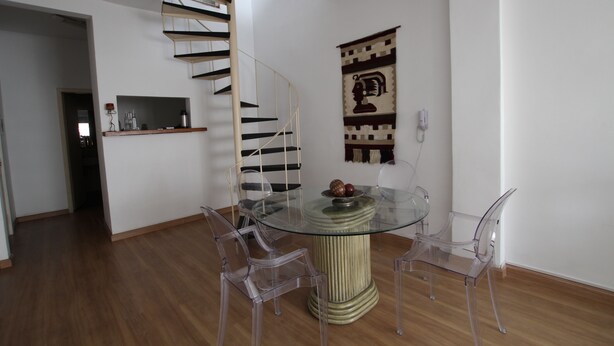 Un coin repas avec une table en verre et quatre chaises transparentes, un escalier en colimaçon et un téléphone fixé au mur.