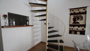 Un escalier en colimaçon dans une pièce dont le sol est en bois, une étagère remplie de bouteilles et une tapisserie ornant le mur.