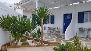 A covered outdoor area with stone flooring, a wooden fence, and potted plants. - Nikos rooms (Mykonos)