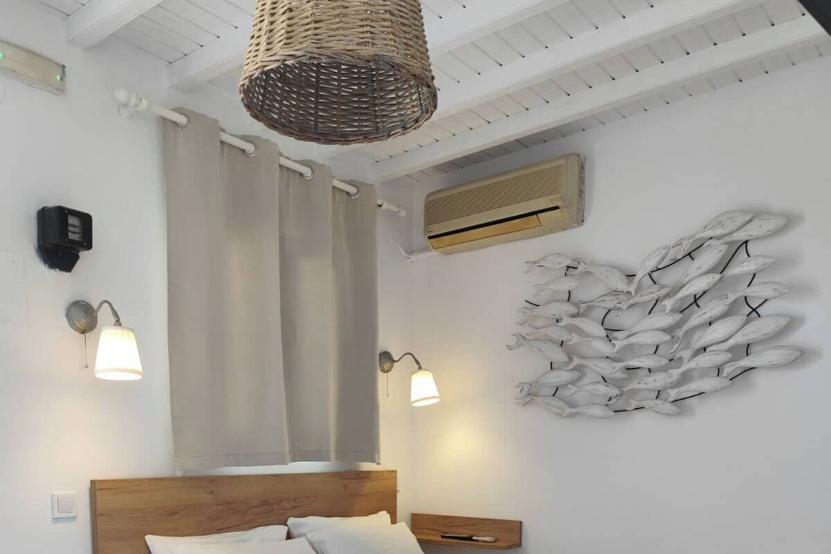 A wooden bed with a quilted pink bedspread, two bedside lamps, a wall-mounted air conditioner, and a decorative wall art piece.