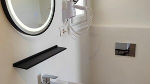 A modern bathroom with a white sink, a round mirror with a black frame, a hairdryer, and a toilet. - Nikos rooms (Mykonos)
