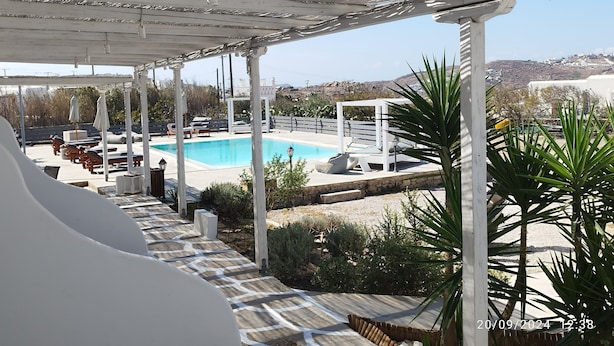 A covered outdoor swimming pool area with lounge chairs and a view of the landscape. - Nikos rooms (Mykonos)