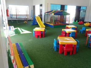 Ein Kinderspielbereich mit Trampolin, Rutsche, Bällebad und Tischen und Stühlen.