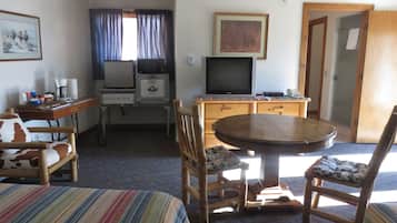 Una habitación de hotel compacta con cama, una pequeña mesa de comedor, televisión, microondas y kitchenette.