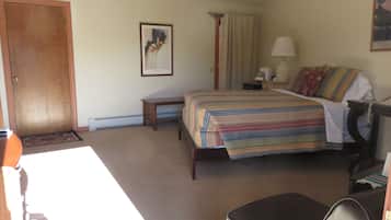 A hotel room with a bed, a bedside table, a lamp, a chair, a door, and a framed picture on the wall.