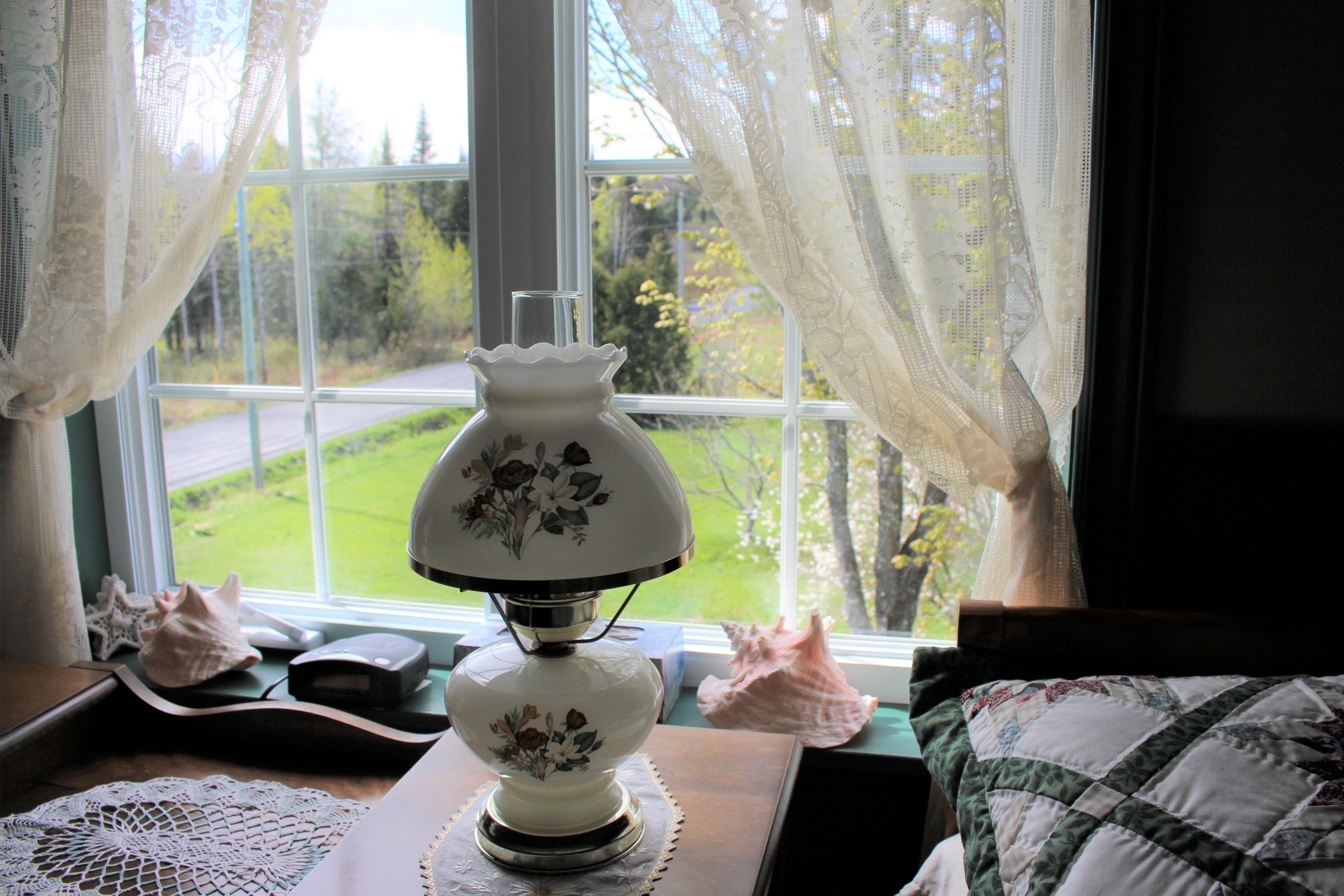A room with a window, a lamp, a doily, a shell, and a quilted pillow.