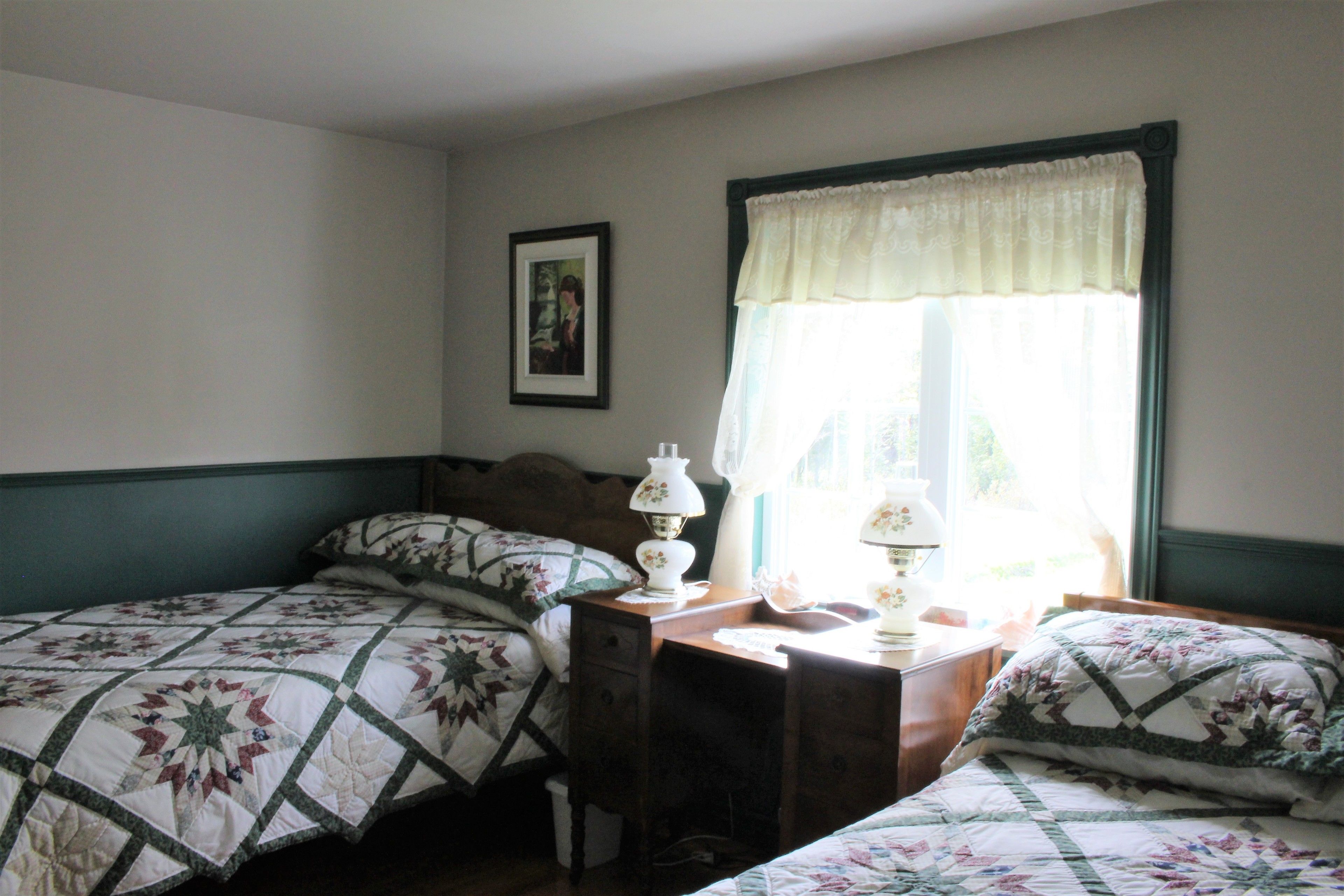 A bedroom with two beds, a nightstand, a lamp, and a window with a curtain.