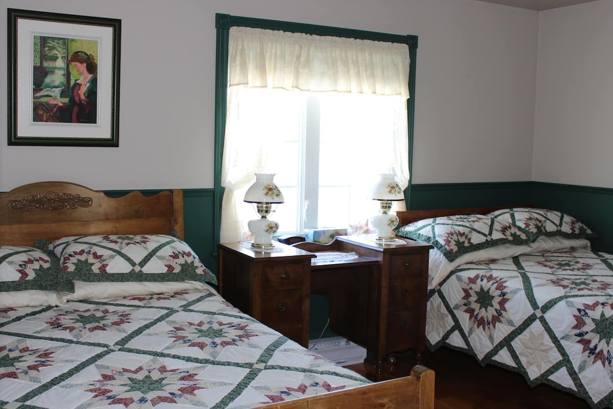 Un dormitorio con dos camas, un escritorio de madera y un ventanal con cortinilla blanca.