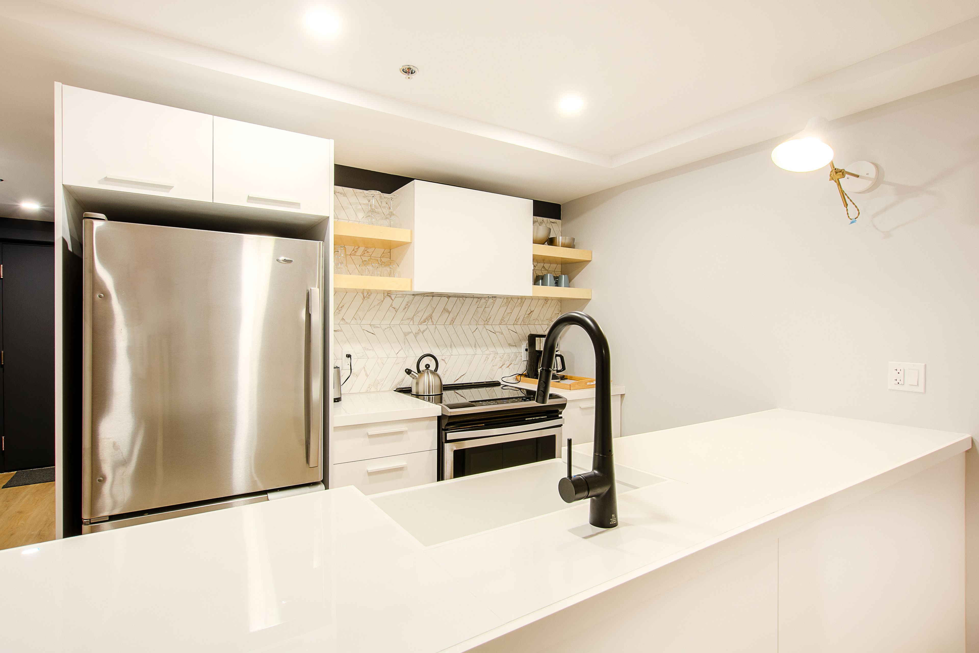 A modern kitchen with a stainless steel refrigerator, white cabinetry, a black faucet, and a marble backsplash.