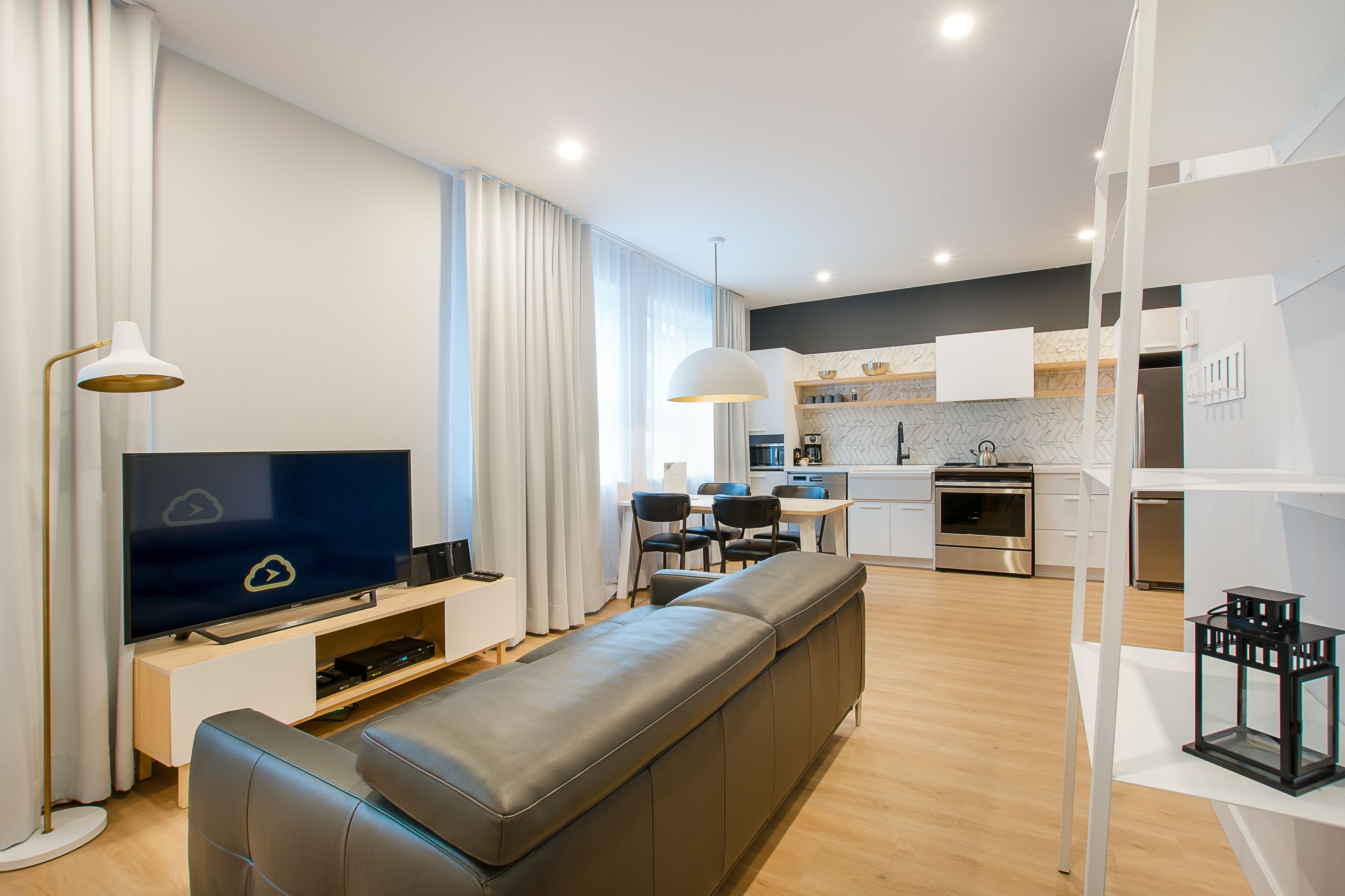 Un salon moderne doté d’un téléviseur à écran plat, d’un canapé, d’un coin repas et d’une cuisine avec des meubles blancs et un plan de travail en bois.