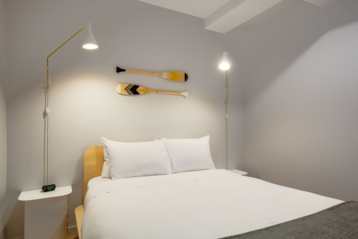 A neatly made bed with white linens, two wall-mounted lamps, and two paddles hanging on the wall.