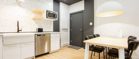 Una cocina moderna con armarios blancos, microondas integrado y un comedor con mesa y sillas.