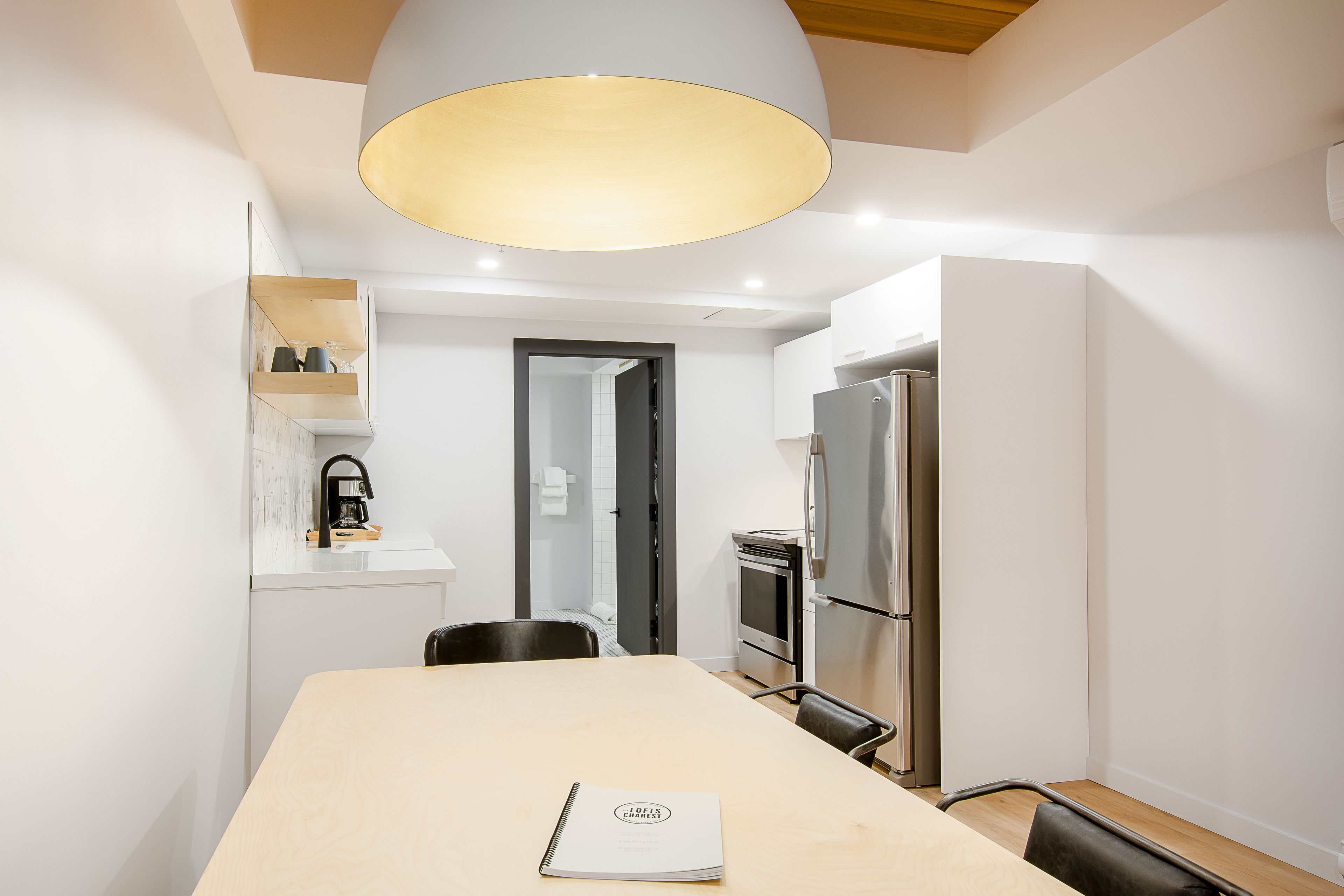 Eine moderne Küche mit Essbereich, ausgestattet mit einem großen Tisch, Stühlen, einem Kühlschrank und einer Pendelleuchte.
