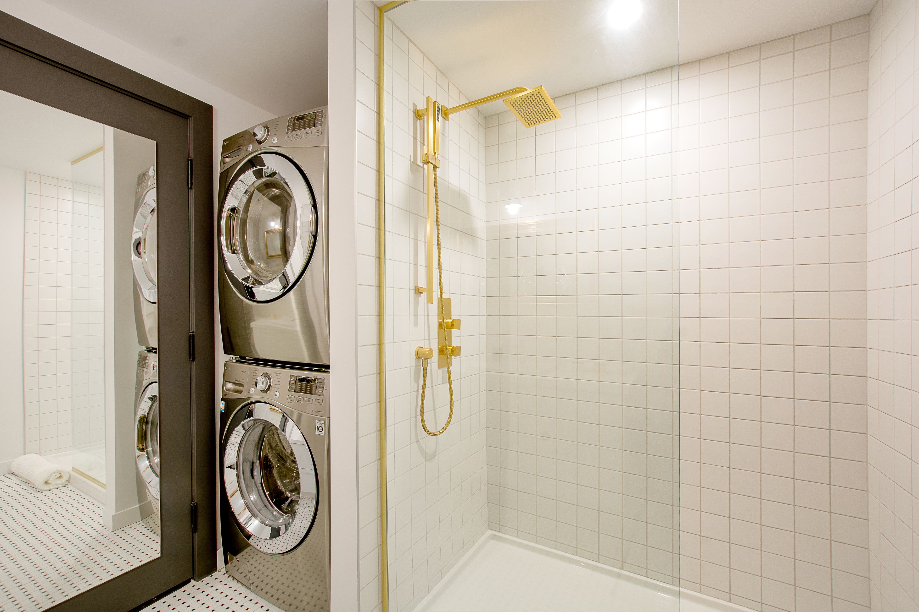 A modern bathroom with a walk-in shower, a double washer and dryer unit, and a large mirror.