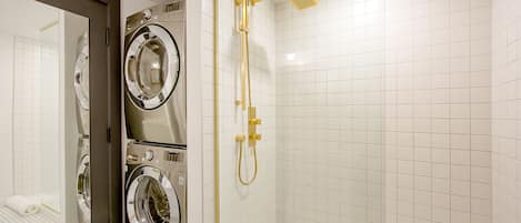 A modern bathroom with a walk-in shower, a double washer and dryer unit, and a large mirror.