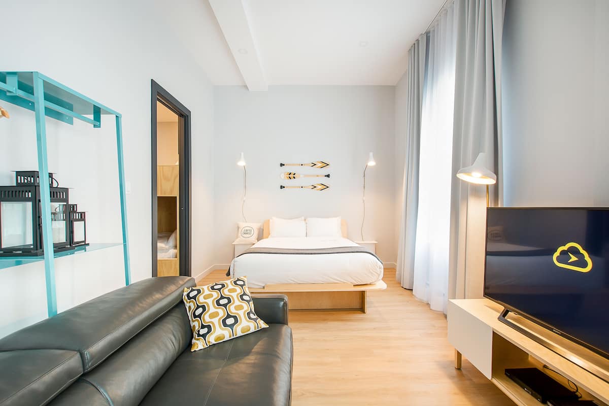 A modern hotel room with a bed, a TV, a sofa, and a desk with a computer.