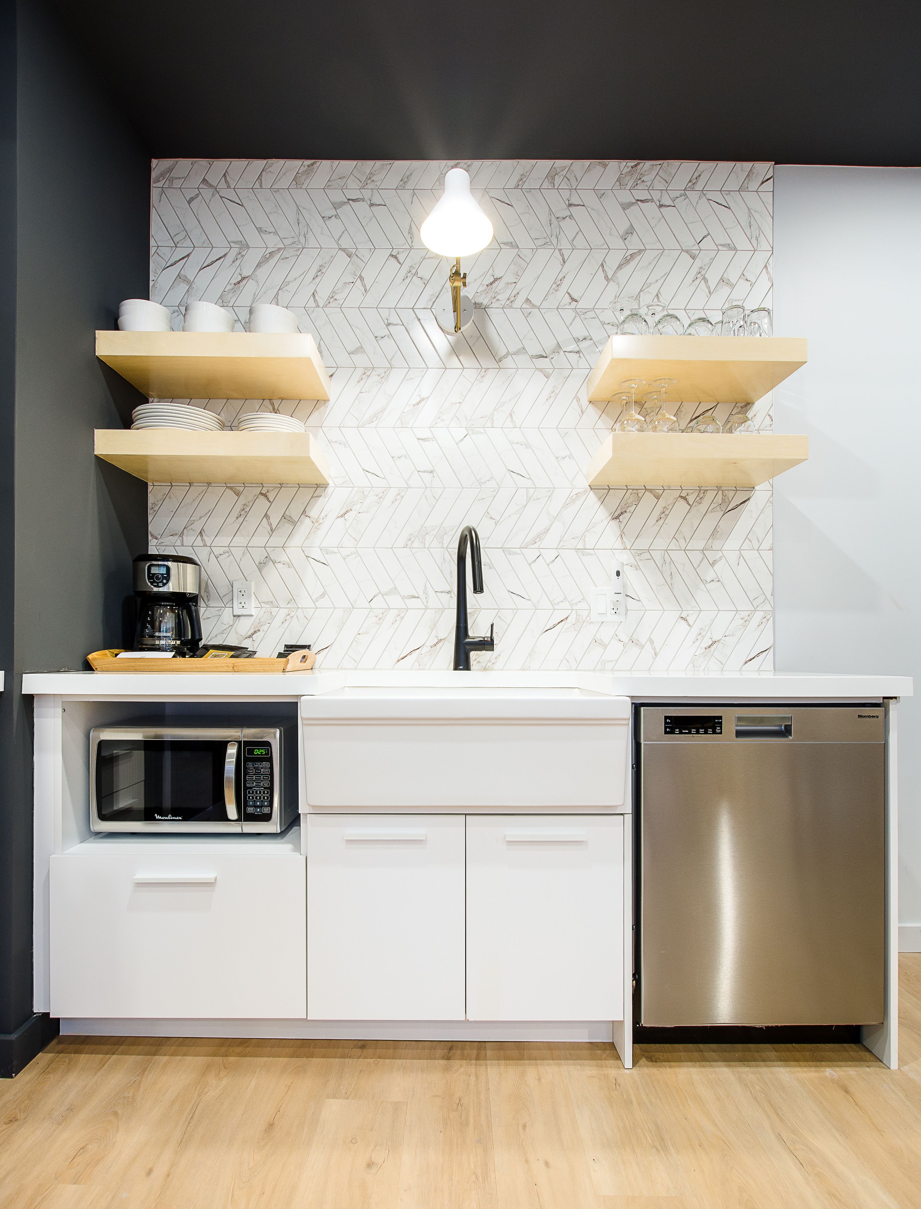 A modern kitchen with a white countertop, a built-in microwave, a dishwasher, and a herringbone-patterned backsplash.