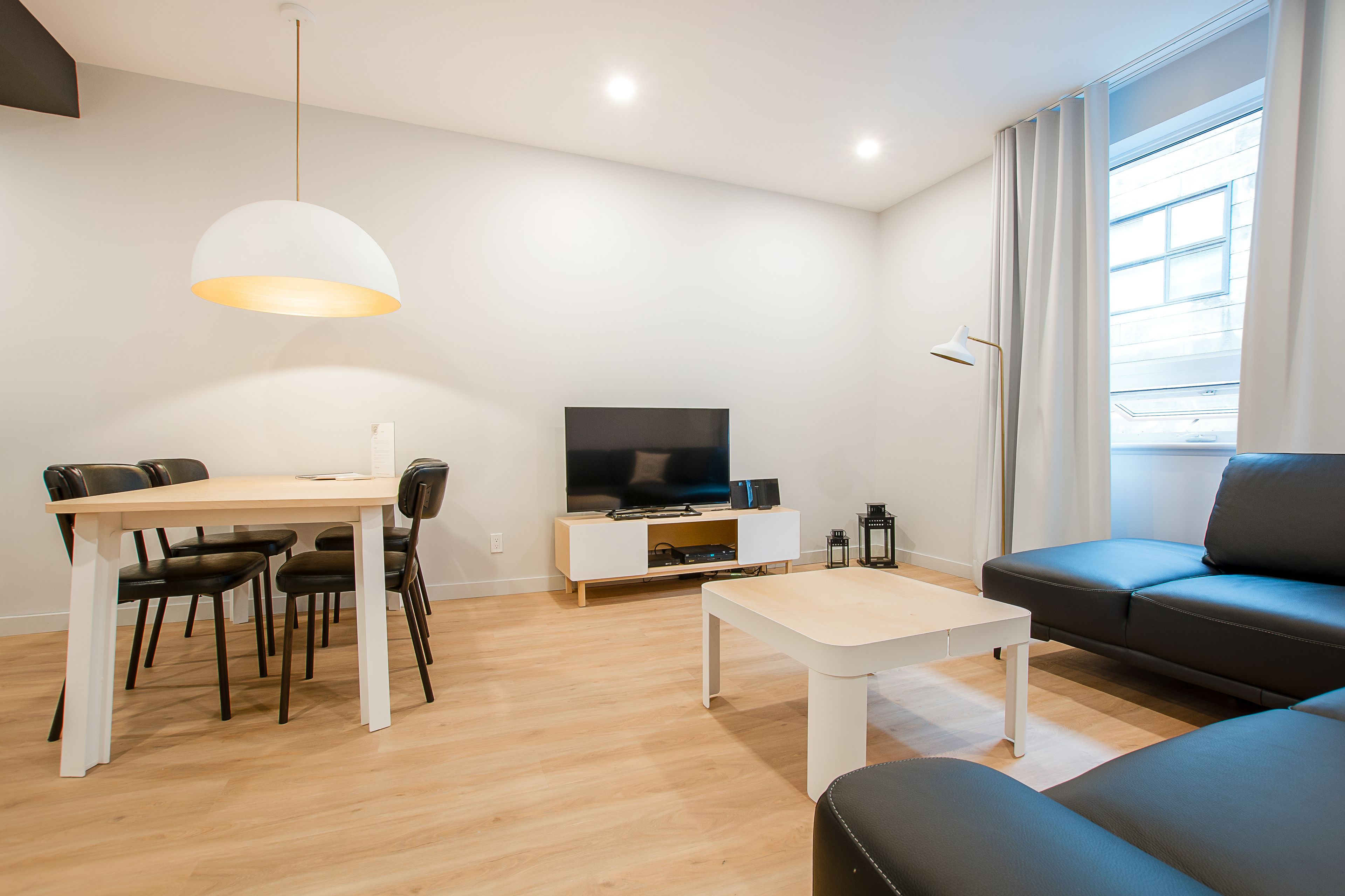 Un salon moderne comprenant un coin repas, un téléviseur à écran plat et une grande fenêtre avec des rideaux.