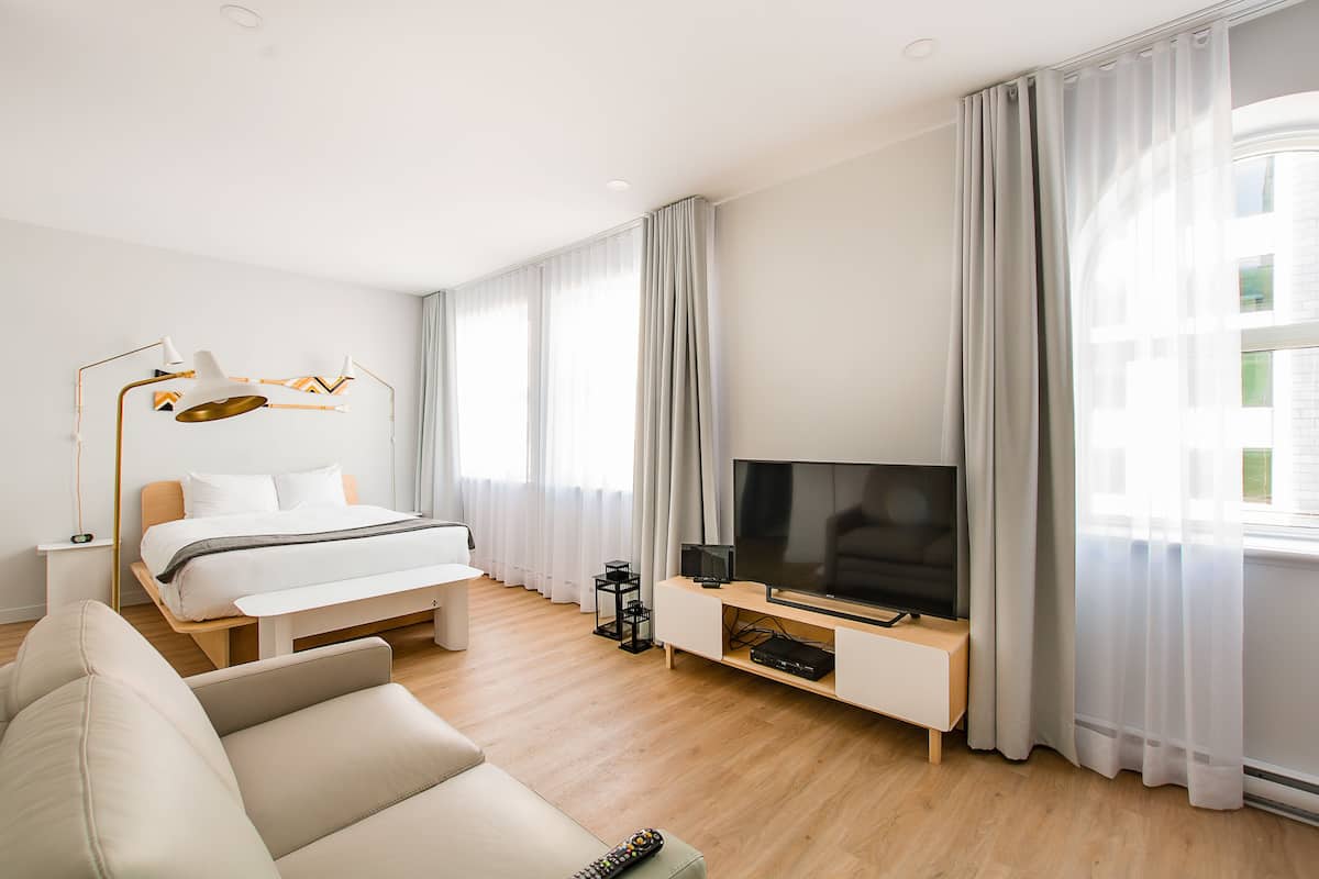 A modern hotel room with a bed, a TV, a sofa, and a desk with a lamp.