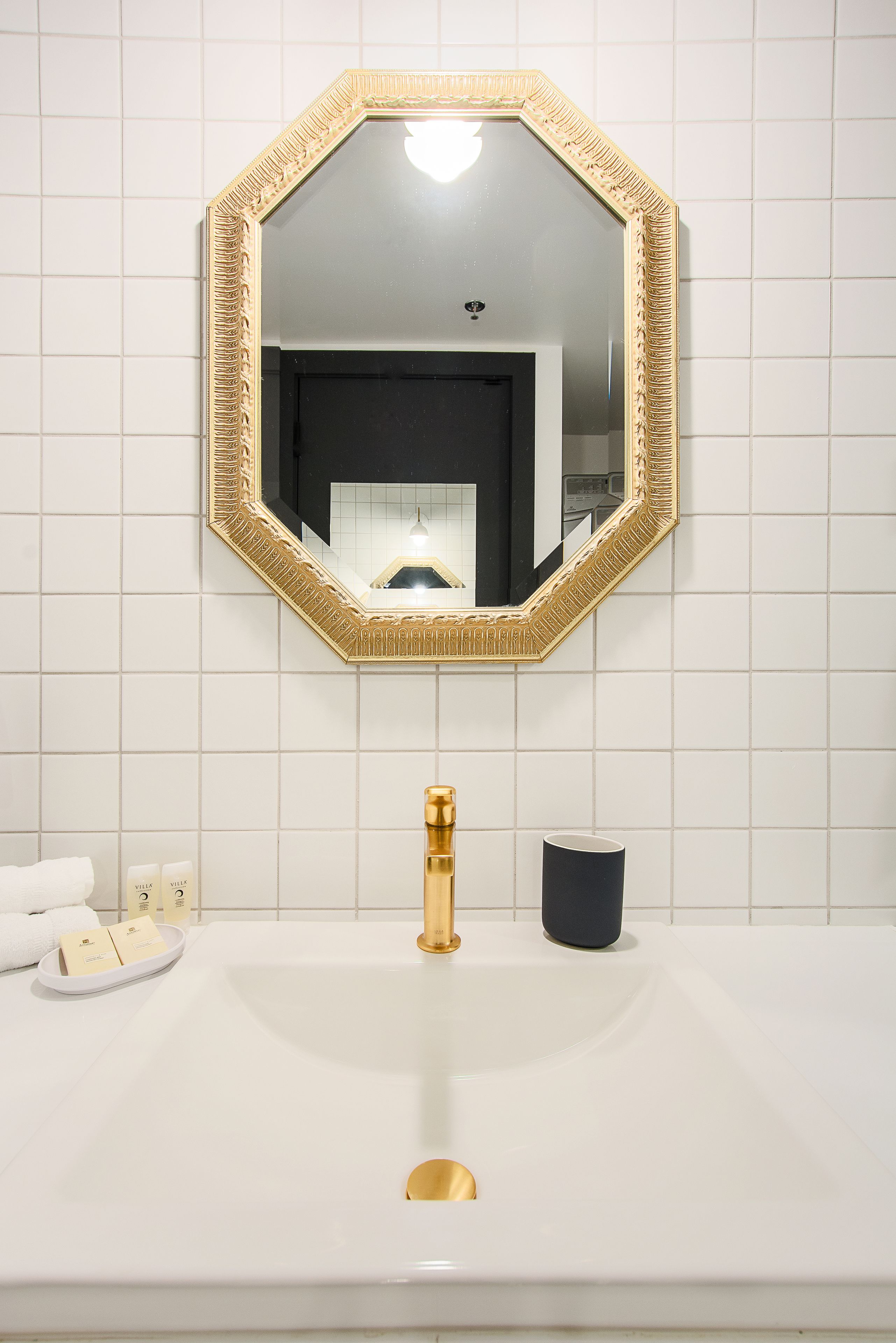 A bathroom with a white sink, gold faucet, and a large mirror with a gold frame.