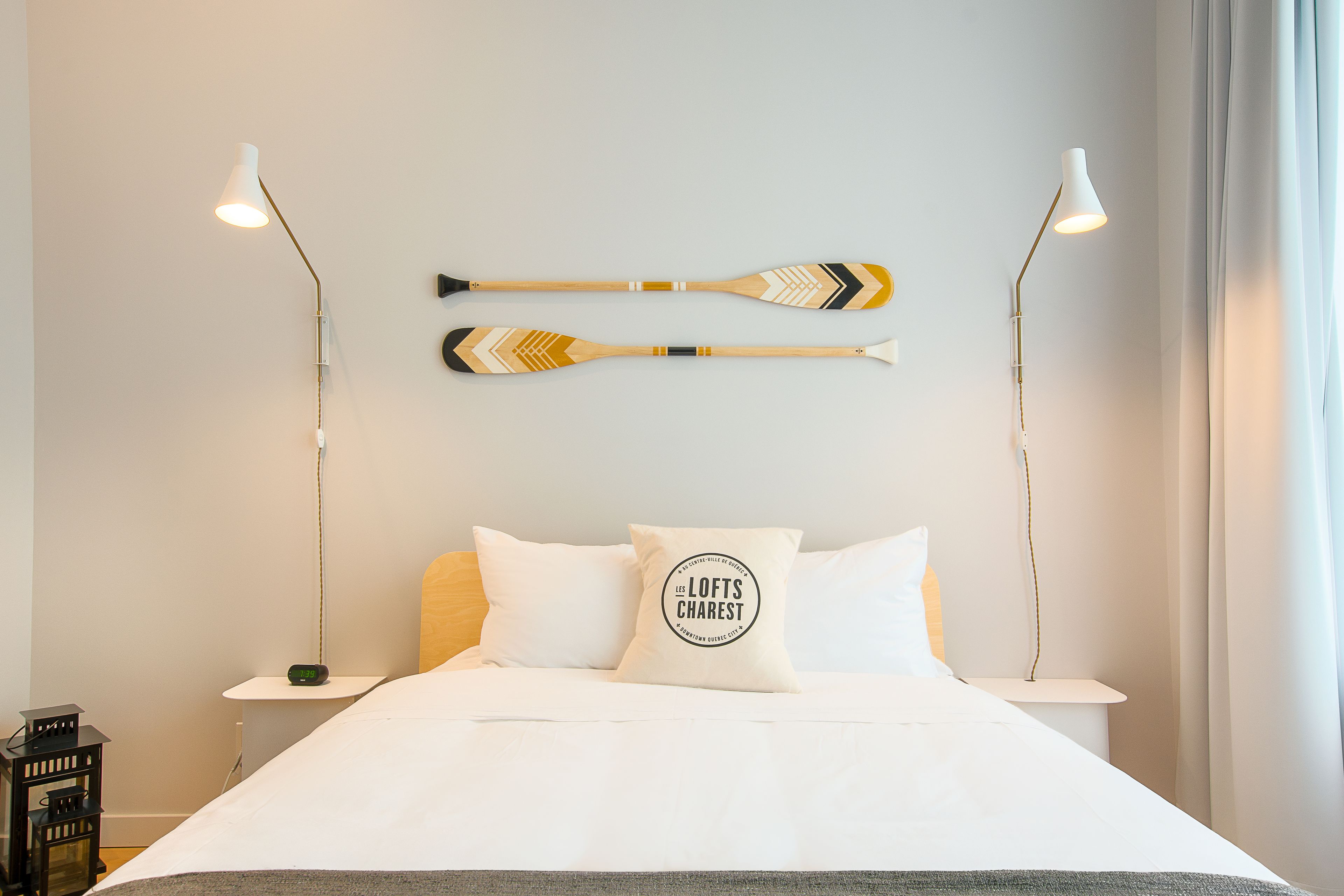 A neatly made bed with white linens, two wall-mounted lamps, and two decorative paddles on the wall.