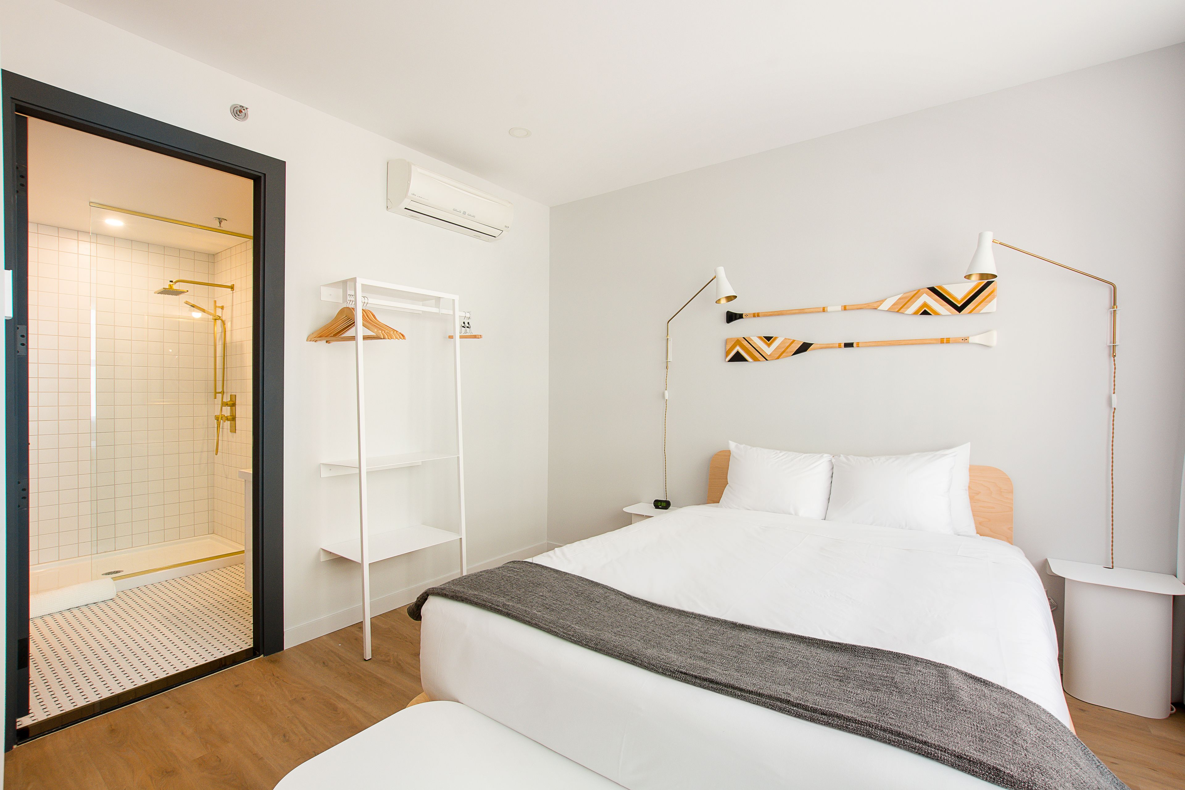 A modern hotel room with a large bed, a walk-in shower, and a bedside table with a lamp.