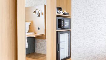 A compact room with a bed, a small desk with a lamp, a microwave, and a refrigerator.