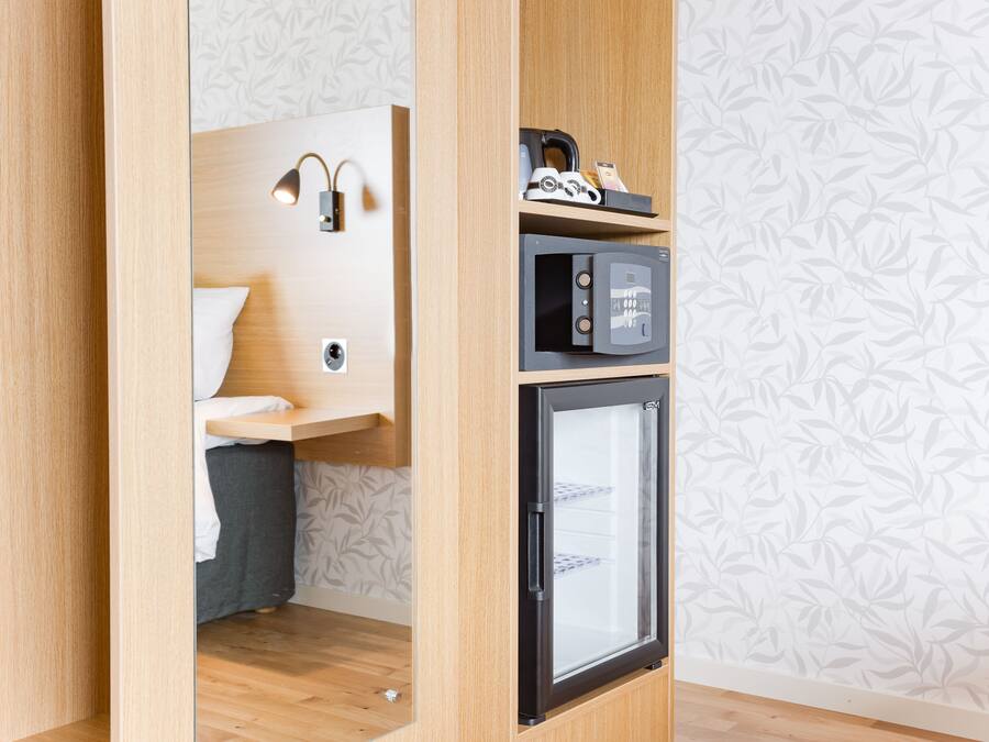 A compact room with a bed, a small desk with a lamp, a microwave, and a refrigerator.