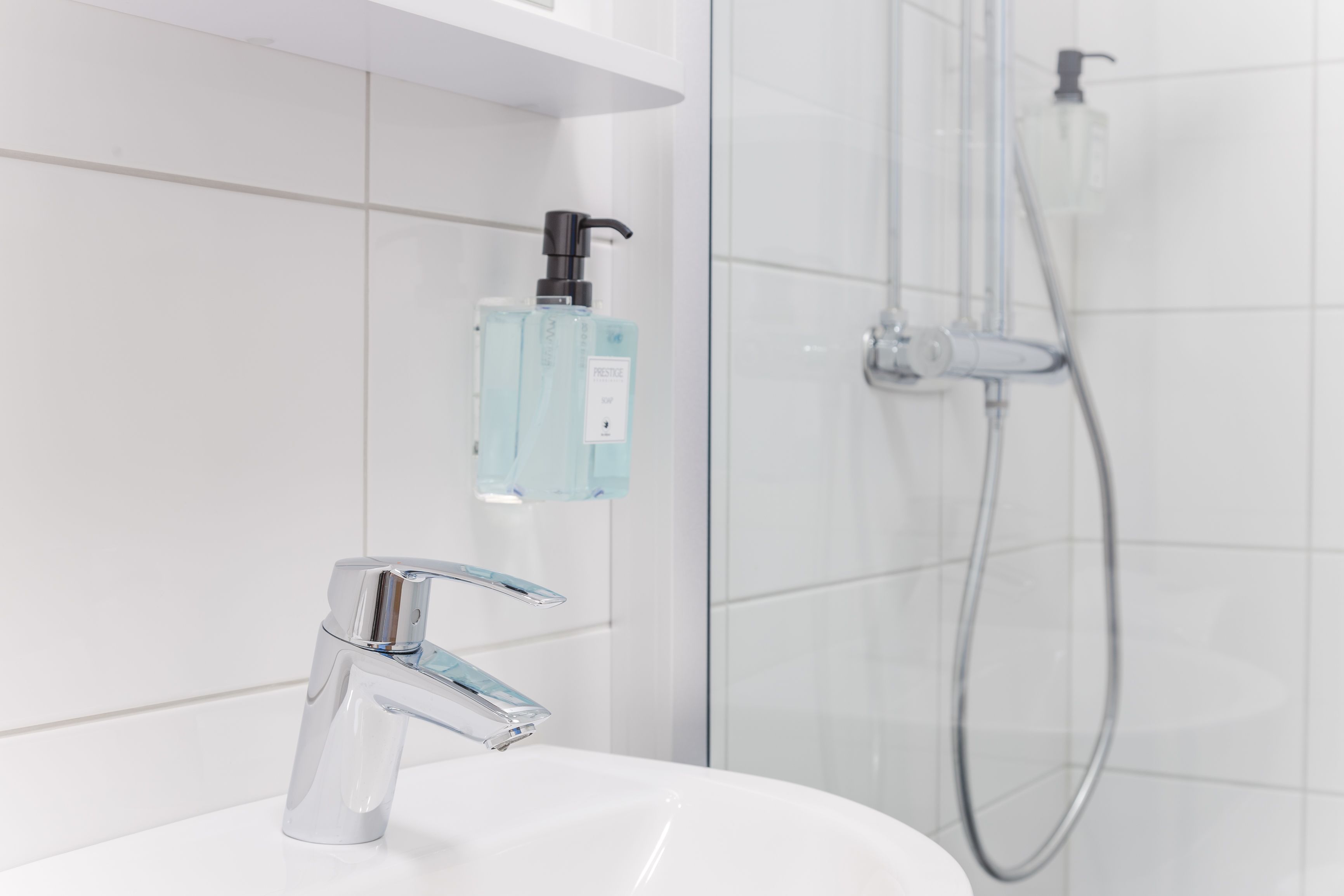 Ein modernes Badezimmer mit chromfarbenem Wasserhahn, einer gläsernen Duschkabine und einem Seifenspender an der Wand.