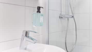 A modern bathroom with a chrome faucet, a glass-enclosed shower, and a soap dispenser on the wall.