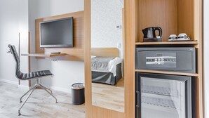 Una habitación de hotel moderna con una cama, un televisor, un escritorio con una silla, una cafetera y un refrigerador pequeño.